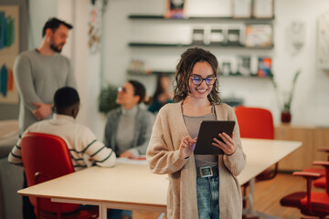 Young businesswoman using digital tablet in modern office with colleagues working in background