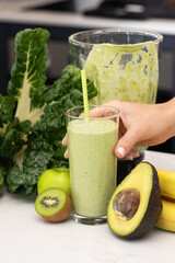 Woman holding glass with green smoothie made from avocado, kiwi and green apple