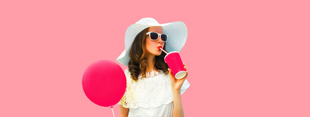 Beautiful young woman model with cup of juice holding balloon summer hat on pink background