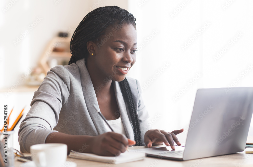 Poster smiling black businesswoman working on laptop and taking notes in modern office. free space for your
