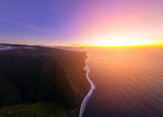 Vibrant sunset illuminates the rugged coastline and vast ocean waters at twilight, showcasing...