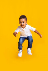 Adorable afro baby boy jumping over yellow studio background with copy space