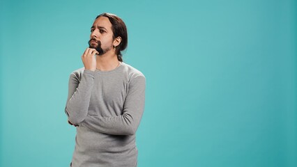 Pensive man deep in thoughts, doing ruminating hand gesturing, isolated over studio background....