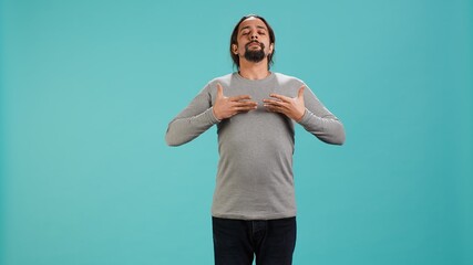 Fototapeta premium Portrait of man inhaling and exhaling to relax and gain positive energy, eliminating stress. Person doing breathing exercises for wellbeing, isolated over studio background, camera A