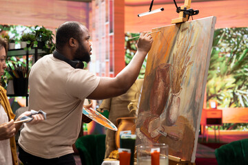 Team of skilled artist collaborating on a rustic painting in art studio, using creative painting techniques with brushes and watercolor paint. Applying multicolored dye with careful brushstrokes.
