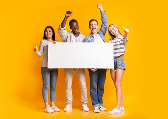 Excited international group of teenagers holding empty white plackard, yellow background