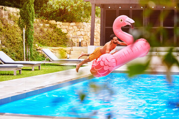 Man, flamingo and jump into pool for swim, luxury and enjoy the summer at resort. Pink float, male person and dive at water with inflatable toy, excitement and energy on weekend trip for vacation © Dean2000/peopleimages.com