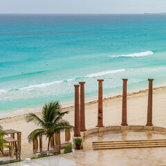 Empty Cancun beach with turquoise waters, palm trees, and ancient-style columns under a rainy morning sky. High-quality photo . Cancun Hotel Zone, Mexico