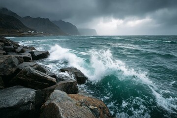 Obraz premium Ocean Waves Crashing Against Rocky Coastline Under Overcast Sky With Mountains and Distant Coastal Buildings