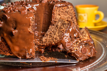 Detail of chocolate cake with syrup and chocolate drops and blurred coffee cup in the background