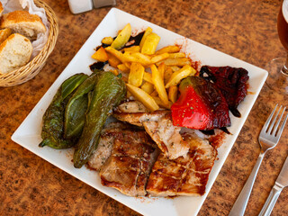 Lunch served on plate - roasted pork chop with stewed vegetable tomatoes, peppers, onion, pieces. Dish garnished by baked vegetables, complemented by French fries