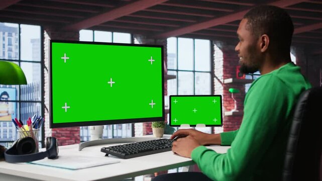 Black male worker in his loft using copy space PC to analyze sales reports and plan business growth, remote job. Young man working from home doing project research, typing on computer. Camera B.