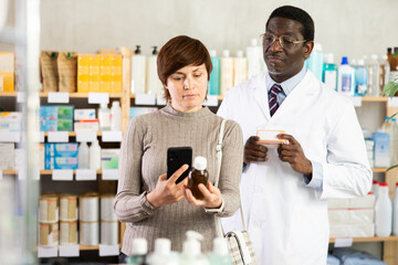 Woman in pharmacy scans QR code on antitussive syrup, studies item in detail, collects information online, uses quick link to access drugs instructions. African man pharmacist offer available