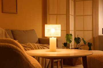 Interior of night living room with sofa, folding screen and glowing lamp on coffee table