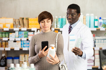 Woman in pharmacy scans QR code atopic cream product, checks certificate on manufacturers website. Client learns information about product, reviews and recommendations for use