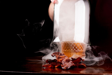 carefully opening smoker with smoked old fashioned cocktail crispy bacon slices in focus