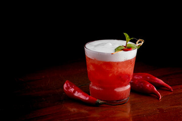 spicy red cocktail with peppers with creamy spicy ginger foam and mint on wooden table