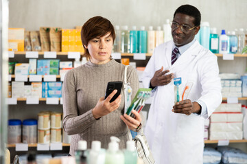 Adult woman buyer scanning qr code for toothbrush with adult man pharmacist in pharmacy