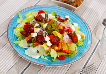 Appetizing salad of fresh vegetables with chorizo, feta avocado and pesto sauce served on platter