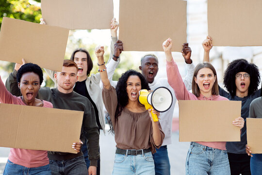 Young mixed race woman with megaphone leading a group of demonstrators with blank placards on the street. International group of people protesting for human rights, showing empty boards
