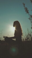 Naklejka premium Silhouette of a woman meditating outdoors during a serene sunset