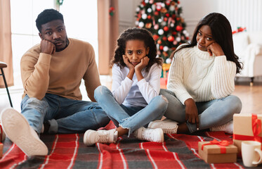 Bored dissatisfied black family disappointed with celebration or Christmas gifts, sitting on floor...