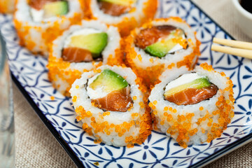 Japanese restaurant serves food - set of California rolls made from of avocado, salmon, cheese and decorated with masago caviar. Widely known East Asian food, oriental restaurant