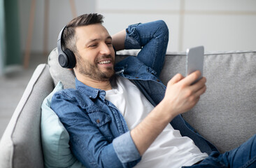 Time to relax. Handsome middle-aged bearded man in wireless headphones listening to music online on...