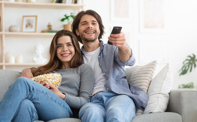 Watching TV at home. Loving couple resting on sofa and eating popcorn, copy space