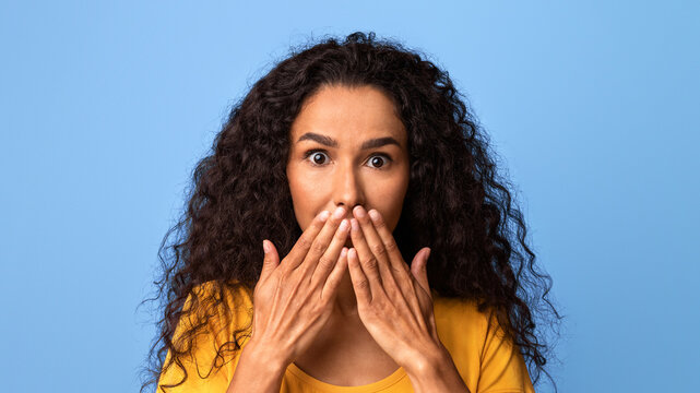 OMG. Shocked Brunette Woman Covering Mouth With Hands, Looking At Camera With Astonishment, Emotionally Reacting To Surprising News, Speachless Lady Posing Over Purple Studio Background, Copy Space