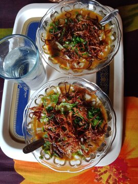 Haleem with spices, herbs mix,  meat, and vegetables salad mix. A glass of water with haleem. 