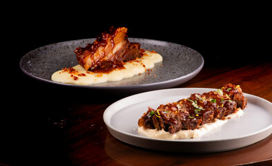 two plates of pork belly in strips and slices under a bed of parmesan cheese