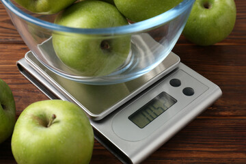 Electronic kitchen scale with bowl of green apples on wooden table, closeup