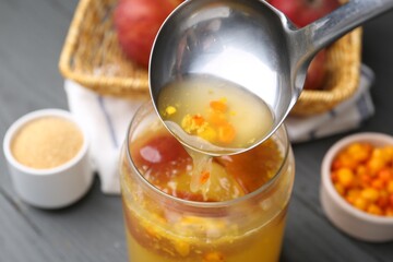 Pouring tasty compot into glass jar on grey wooden table, closeup