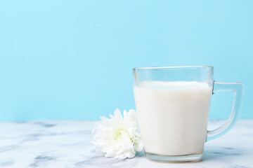 Cup of milk and flower on white marble table against light blue background. Space for text