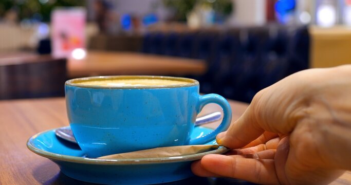 Professional barista serving freshly prepared cappuccino in light blue ceramic cup on rustic wooden surface within modern, stylish cafe interior. Concept of coffee consumption - Powered by Adobe
