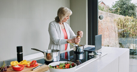 Mature woman, cooking and laptop in kitchen with healthy food, recipe or reading a blog for dinner. Vegetarian, diet and person in home prepare vegetables, salad and nutrition with salt in meal