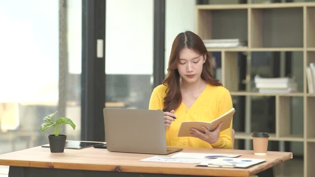 Focused Young Asian Businesswoman Writing in Notebook at Office Desk