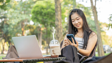 Young girl using mobile phone and laptop in the park