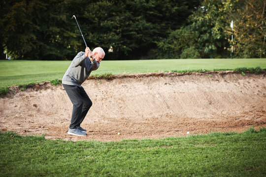 Golf, bunker and man golfer playing with ball and metal club on outdoor pitch or field. Sports, sand and senior male athlete hitting equipment on outside course for match, training or game practice. - Powered by Adobe