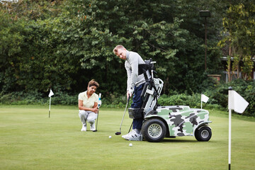 Golf cart, sports and person with disability playing on a field for outdoor hobby, leisure or practice for game. Nature, equipment and people training with balls, clubs and flags on grass course.