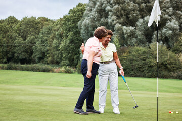 Fototapeta premium Senior women, golf and holiday with hug, celebration and outdoor on a course and lawn. Fitness, club and field with sport, health and wellness with smile and target practice on vacation on grass