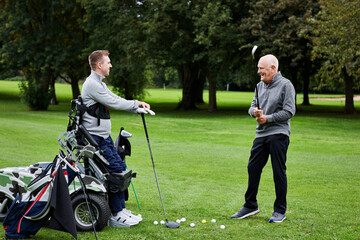 Sports, friends and men on field for golf in game, match and competition on golfing course. Recreation, talking and senior man with person with disability with club for training, fitness and practice