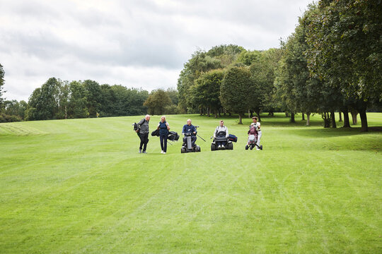 Person, golf cart and mobility aid with group on field for paragolfer or adaptive sports, teamwork or walking. People, support and lawn for competition as country club for health, hobby or recreation