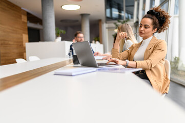 Serious businesswoman holding glasses and thinking seriously while working online over laptop in board room