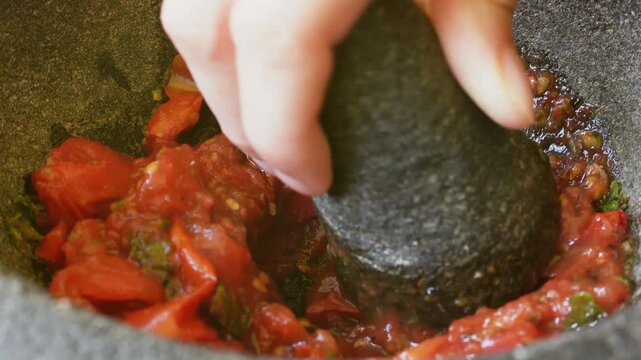 Acercamiento a preparaci&oacute;n  salsa en molcajete, moliendo los tomates asados
