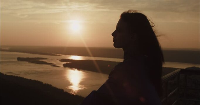 Woman watching sunset over river from mountain top