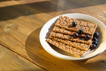 Crisp bread is artfully arranged on a plate with fresh berries, placed on a rustic wooden table, illuminated by warm sunlight.