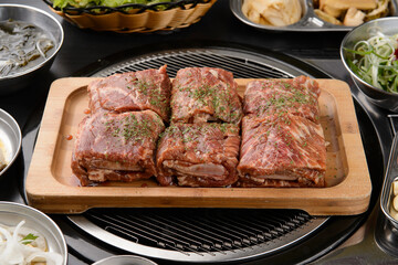 Six pieces of seasoned ribs are rolled up on a wooden plate.
