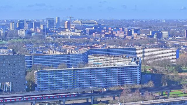Aerial: Johan Cruyff Arena, cityscape and trains during the day in Amsterdam, Netherlands, establishing drone shot